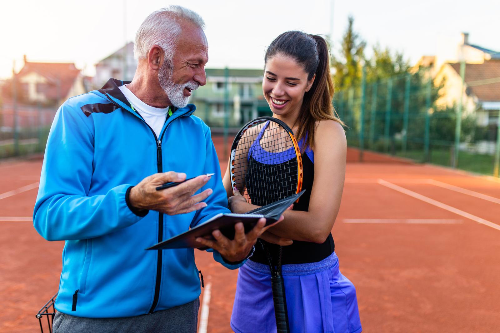 Young tennis player talking with her coach on court